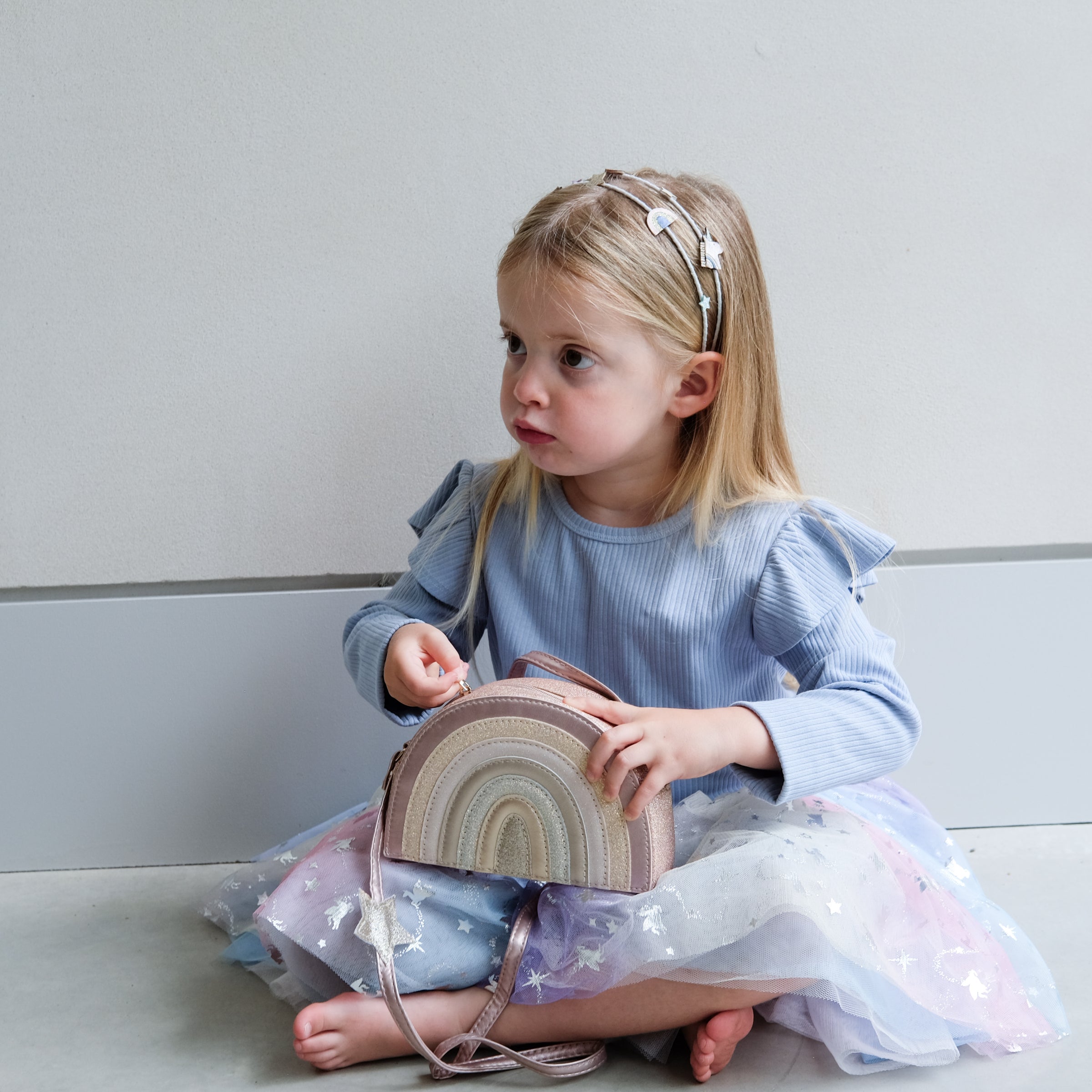 Young girl holding a rainbow-shaped bag against a plain background