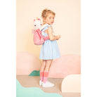 Young girl holding a plush unicorn backpack against a pastel-colored background