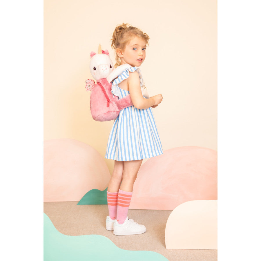 Young girl holding a plush unicorn backpack against a pastel-colored background