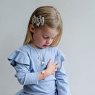 Young girl wearing a blue sweater and unicorn jewellery with a neutral background